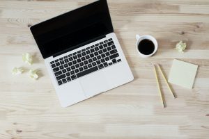 a laptop with crumpled balls of paper, cup of coffee, pencils, and notepad