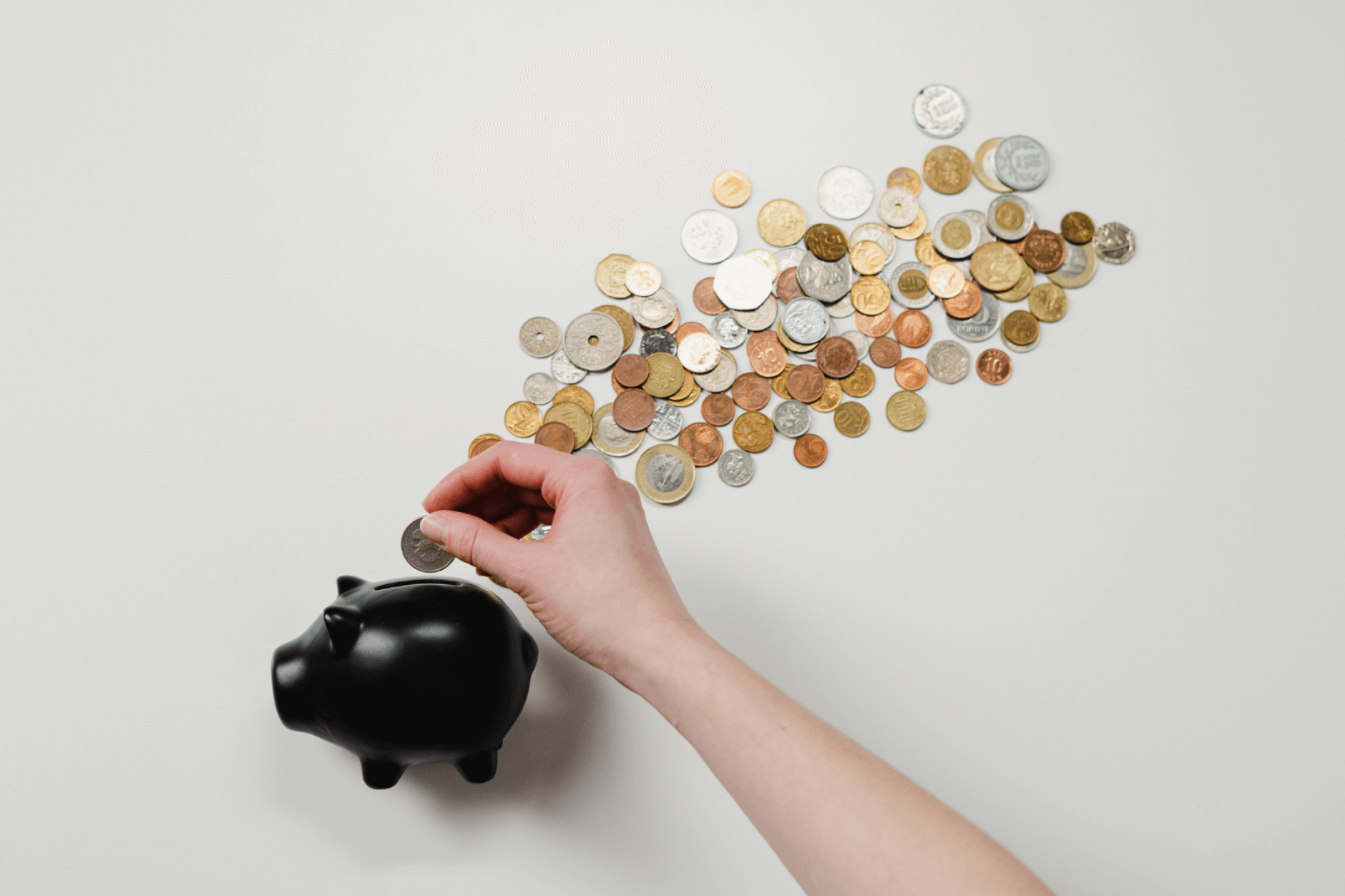 hand putting coin into piggy bank with coins around it